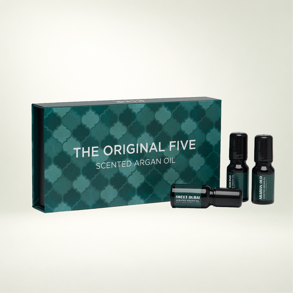Three small dark glass bottles beside a teal patterned box labeled THE ORIGINAL FIVE SCENTED ARGAN OIL.